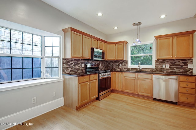 kitchen with sink, tasteful backsplash, hanging light fixtures, light hardwood / wood-style flooring, and stainless steel appliances