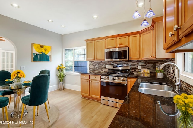 kitchen featuring sink, pendant lighting, stainless steel appliances, light hardwood / wood-style floors, and decorative backsplash