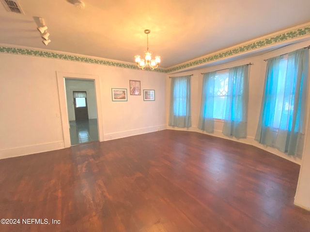 spare room featuring dark hardwood / wood-style flooring, ornamental molding, and a notable chandelier