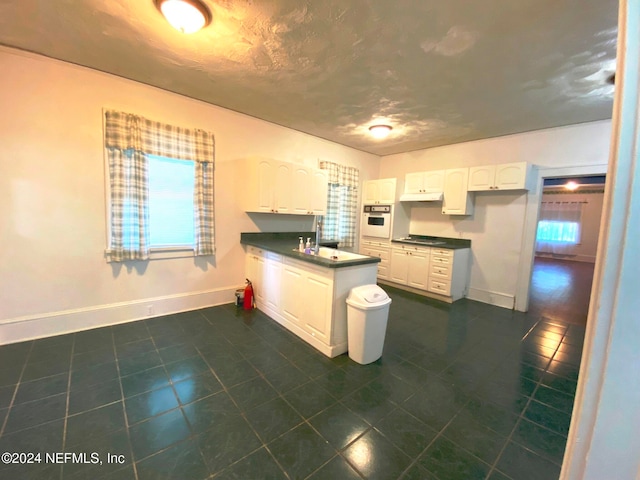 kitchen featuring white cabinets, oven, cooktop, and dark tile patterned flooring