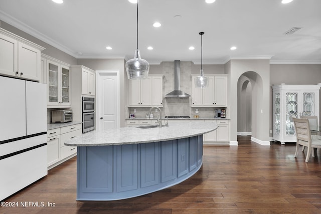 kitchen with wall chimney range hood, appliances with stainless steel finishes, light stone countertops, and hanging light fixtures