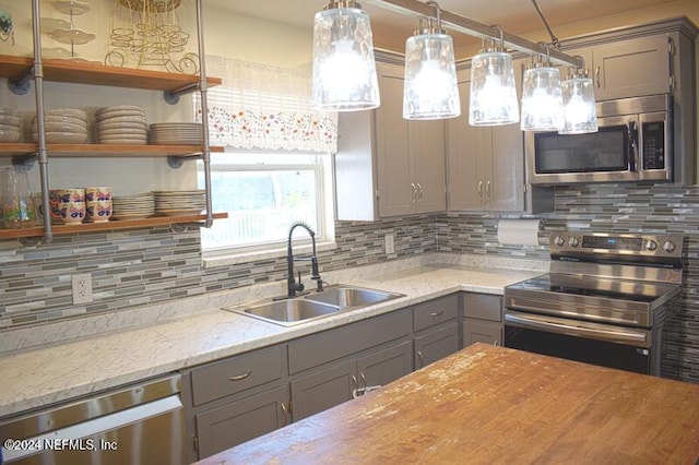 kitchen with sink, hanging light fixtures, stainless steel appliances, light stone counters, and decorative backsplash