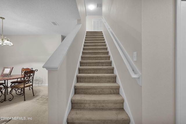 stairs featuring carpet, a textured ceiling, and an inviting chandelier