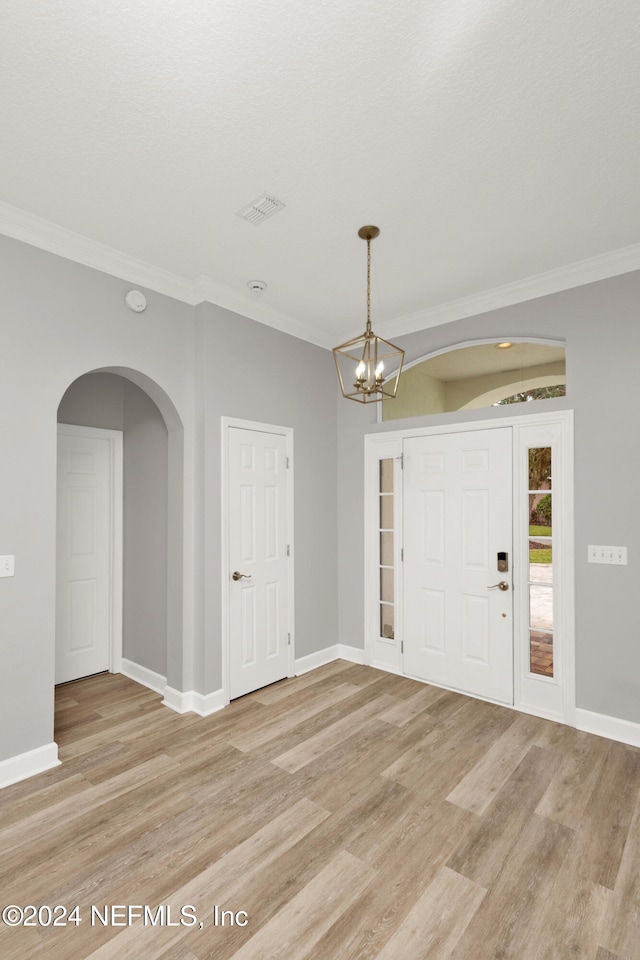 entryway with a chandelier, light wood-type flooring, and ornamental molding