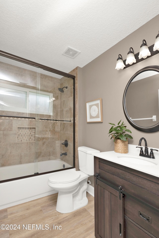 full bathroom with toilet, hardwood / wood-style floors, a textured ceiling, combined bath / shower with glass door, and vanity