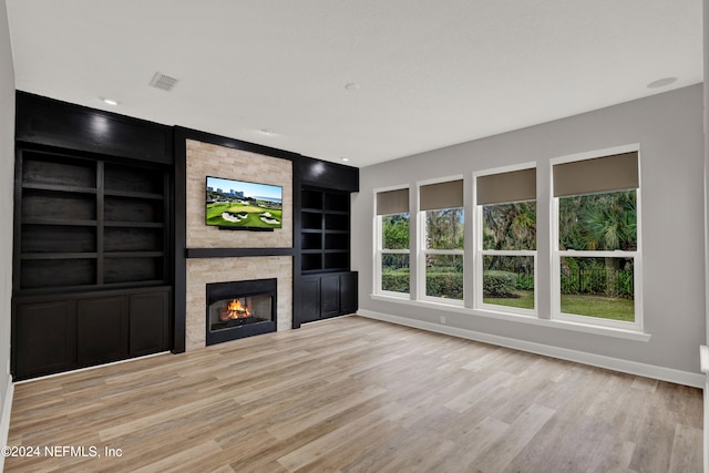 unfurnished living room featuring built in shelves, light hardwood / wood-style floors, and a fireplace