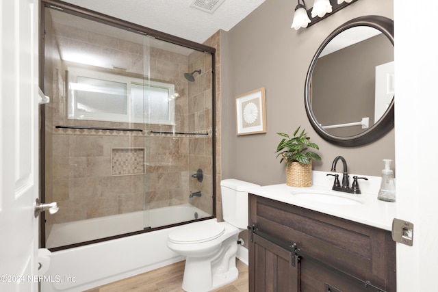 full bathroom with wood-type flooring, toilet, bath / shower combo with glass door, a textured ceiling, and vanity