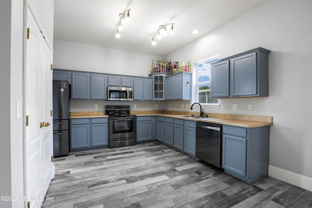 kitchen featuring sink, appliances with stainless steel finishes, a textured ceiling, blue cabinetry, and light wood-type flooring