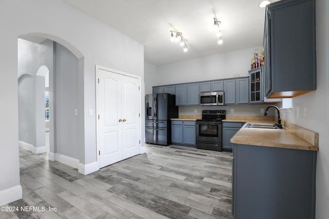 kitchen with a textured ceiling, sink, light wood-type flooring, and appliances with stainless steel finishes