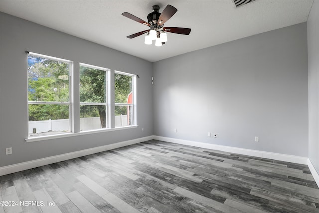 empty room with a textured ceiling, wood-type flooring, a healthy amount of sunlight, and ceiling fan