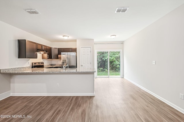 kitchen featuring kitchen peninsula, light stone counters, light hardwood / wood-style floors, dark brown cabinetry, and stainless steel appliances