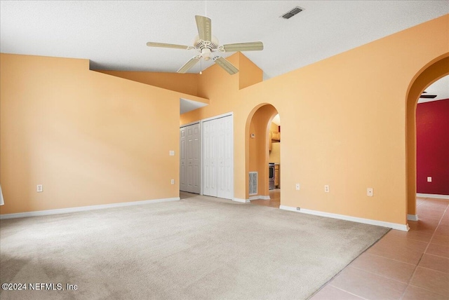 spare room featuring arched walkways, ceiling fan, baseboards, light tile patterned floors, and light carpet