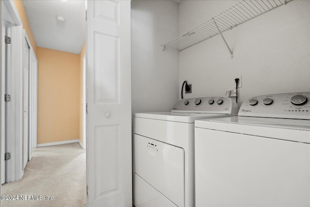 laundry room with light carpet, washer and dryer, and a textured ceiling