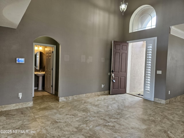 foyer featuring a chandelier, arched walkways, baseboards, and a high ceiling