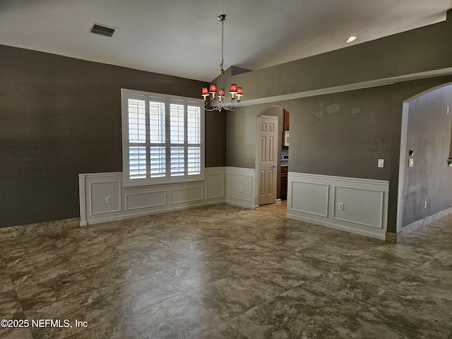 unfurnished dining area with arched walkways, a wainscoted wall, visible vents, a decorative wall, and vaulted ceiling