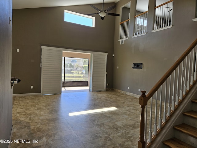 foyer entrance featuring ceiling fan, stairway, a towering ceiling, and baseboards