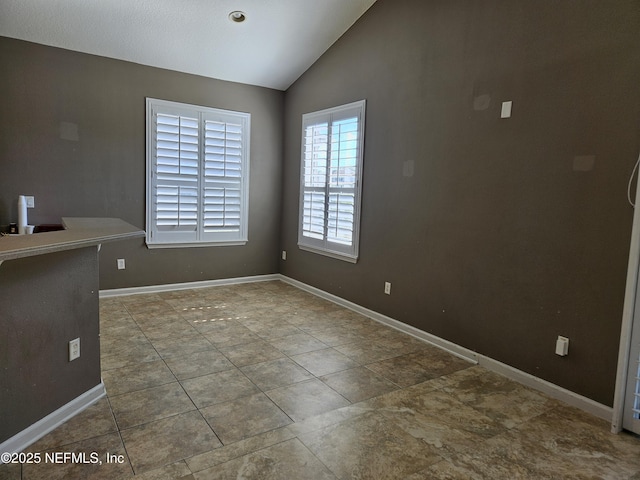 empty room featuring tile patterned flooring, baseboards, and vaulted ceiling