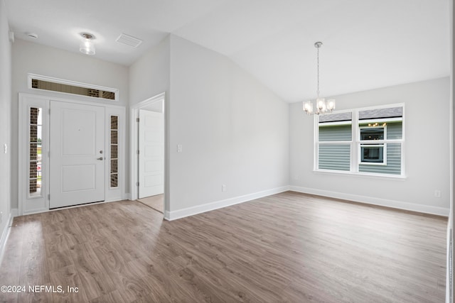 entryway with a healthy amount of sunlight, light wood finished floors, vaulted ceiling, and a notable chandelier