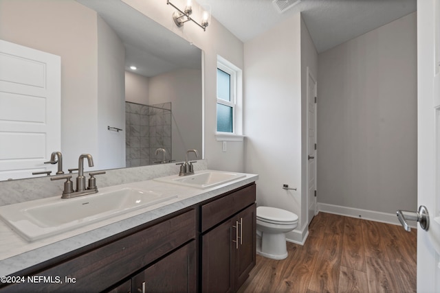 full bathroom with visible vents, a tile shower, a sink, and wood finished floors