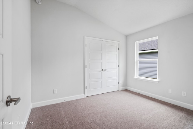 unfurnished bedroom with a closet, carpet flooring, vaulted ceiling, and baseboards