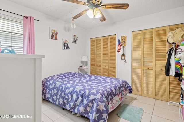 tiled bedroom featuring two closets, a textured ceiling, and ceiling fan