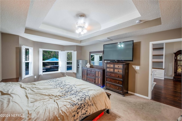 carpeted bedroom featuring ceiling fan, a raised ceiling, a walk in closet, and a textured ceiling