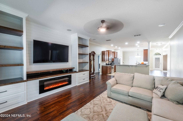 living room with a textured ceiling, ceiling fan, ornamental molding, and dark wood-type flooring