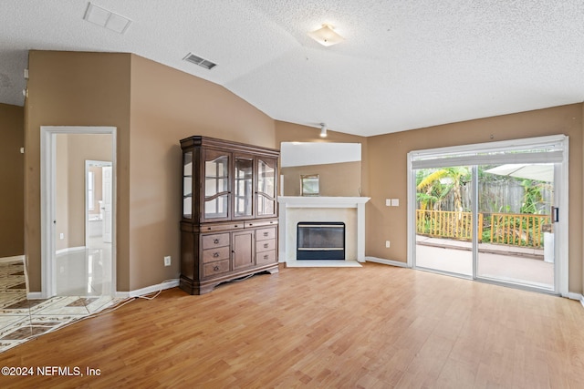 unfurnished living room with light hardwood / wood-style floors, a textured ceiling, and vaulted ceiling