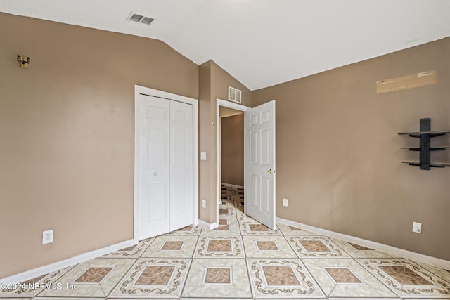 unfurnished bedroom with a closet, light tile patterned floors, and vaulted ceiling