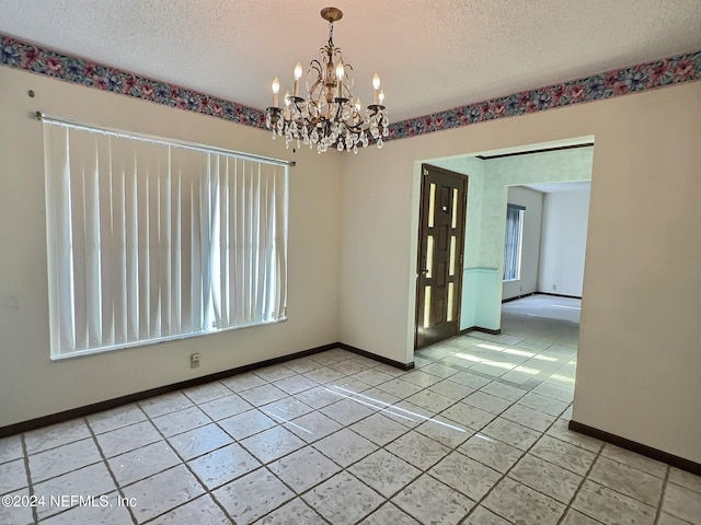 tiled spare room featuring a notable chandelier and a textured ceiling