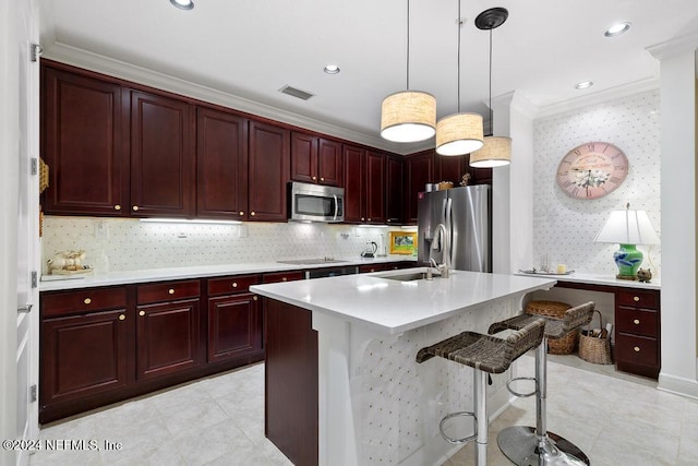 kitchen featuring a breakfast bar, sink, decorative light fixtures, stainless steel appliances, and an island with sink