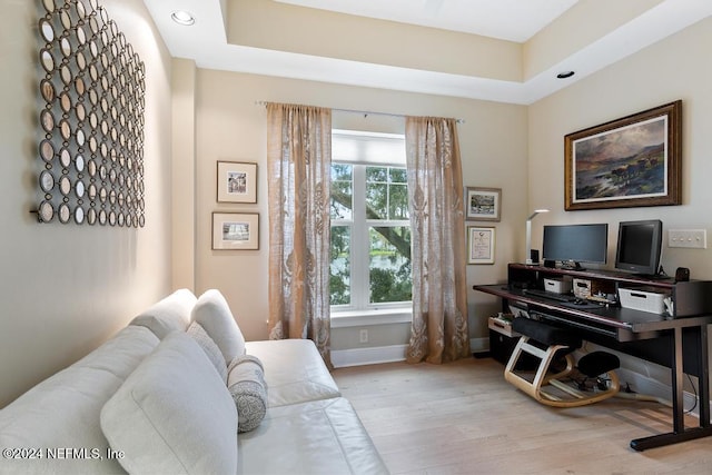 home office with a tray ceiling and light hardwood / wood-style flooring