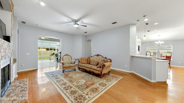 living room with light hardwood / wood-style floors, a stone fireplace, sink, a textured ceiling, and ceiling fan with notable chandelier