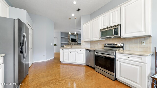 kitchen featuring light wood-type flooring, appliances with stainless steel finishes, pendant lighting, and white cabinetry