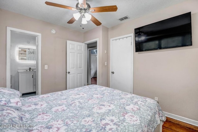 bedroom featuring ensuite bath, a textured ceiling, ceiling fan, hardwood / wood-style flooring, and a closet