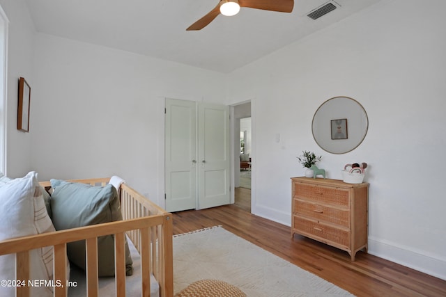 bedroom with ceiling fan, hardwood / wood-style flooring, and a nursery area