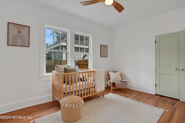 bedroom featuring ceiling fan, a crib, and hardwood / wood-style floors