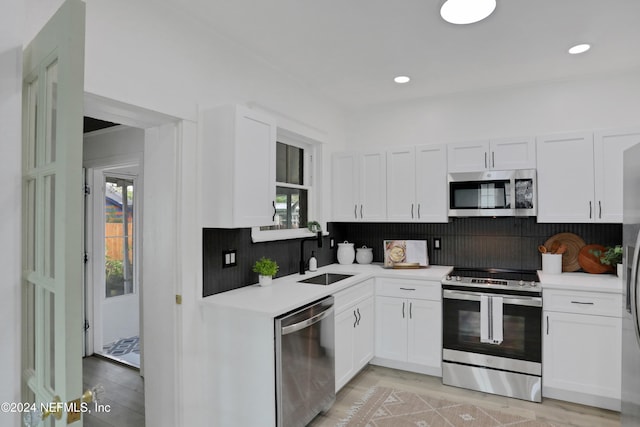 kitchen featuring stainless steel appliances, sink, white cabinetry, light hardwood / wood-style floors, and tasteful backsplash