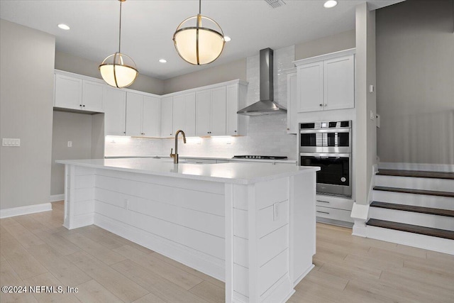 kitchen featuring wall chimney exhaust hood, a center island with sink, and white cabinets