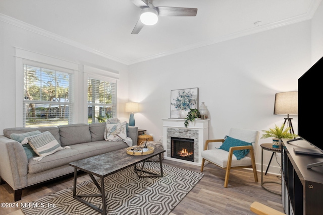 living room featuring ceiling fan, a stone fireplace, ornamental molding, and hardwood / wood-style floors