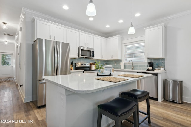 kitchen featuring appliances with stainless steel finishes, a kitchen island, decorative light fixtures, white cabinets, and light hardwood / wood-style flooring