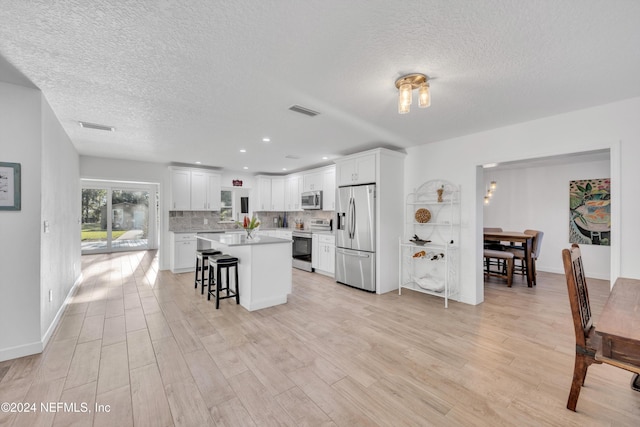 kitchen featuring a breakfast bar area, white cabinetry, stainless steel appliances, and light wood-type flooring