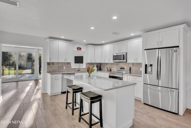 kitchen with a kitchen island, light hardwood / wood-style flooring, a breakfast bar, white cabinetry, and appliances with stainless steel finishes