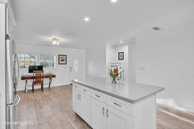 kitchen with a center island, light hardwood / wood-style flooring, white cabinets, and stainless steel refrigerator