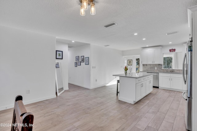 kitchen featuring white cabinets, a kitchen island, appliances with stainless steel finishes, a textured ceiling, and light wood-type flooring