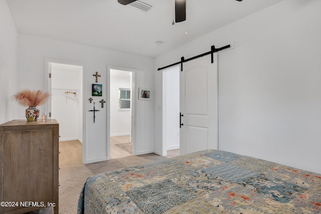 carpeted bedroom with ceiling fan, ensuite bath, and a barn door