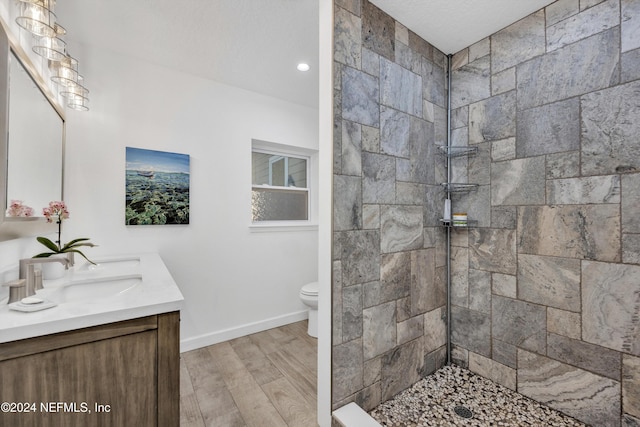 bathroom with a textured ceiling, toilet, tiled shower, vanity, and hardwood / wood-style flooring