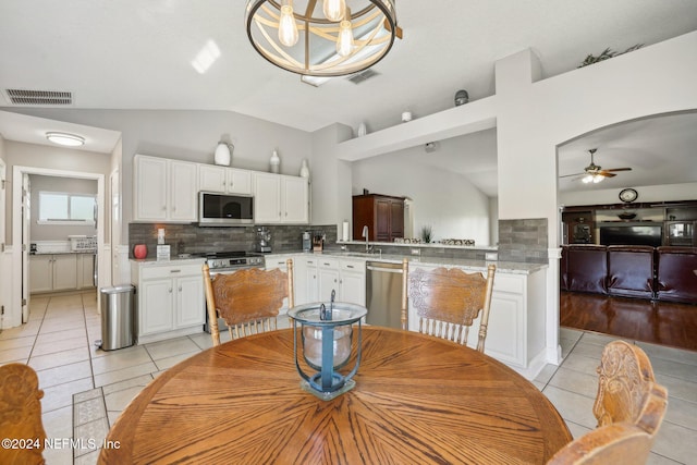 tiled dining room with sink, vaulted ceiling, and ceiling fan with notable chandelier