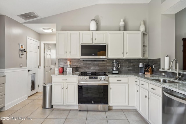 kitchen featuring light stone countertops, backsplash, stainless steel appliances, lofted ceiling, and white cabinets