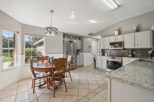 kitchen with stainless steel appliances, backsplash, sink, light stone countertops, and pendant lighting